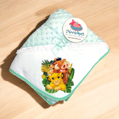 Manta de bebé azul claro com personagens do Rei Leão e etiqueta Pirralhos sobre superfície de madeira