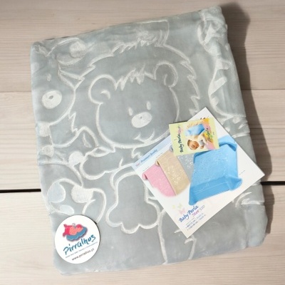 Manta cinzenta com padrão de urso em relevo e etiqueta de marca sobre madeira clara