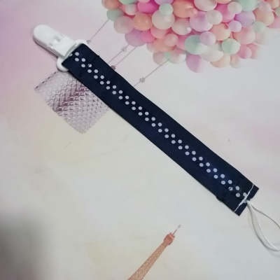 Prendedor de chupeta azul escuro com formas brancas numa superfície com balões coloridos