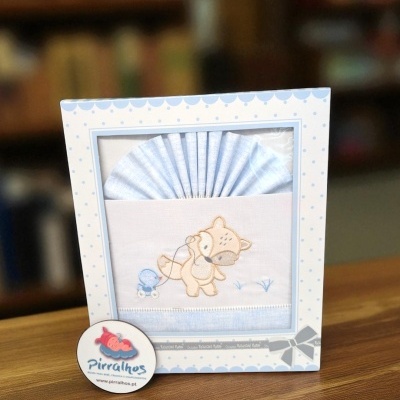 Conjunto para bebé azul claro e branco com bordado de cão numa caixa decorada.