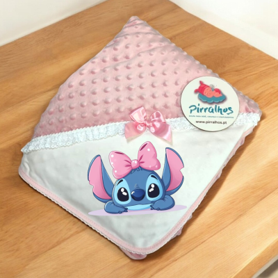Manta rosa para bebé com personagem Stitch e laço cor de rosa numa superfície de madeira