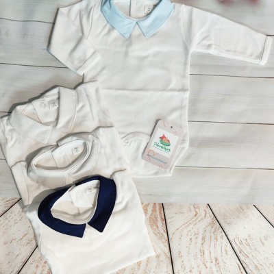 Bodies de bebé branco com golas coloridas e decoração de corações em tecido vermelho e branco ao fundo