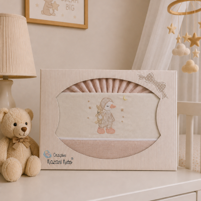 Conjunto de roupa de bebé cor de rosa embalado numa caixa decorada, sobre uma cómoda, ao lado de urso de peluche e lâmpada