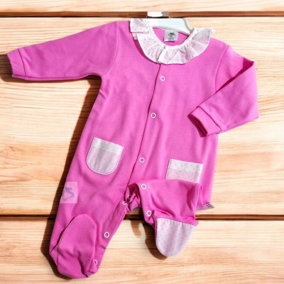 Macacão rosa de bebé com gola branca e bolsos, colocado sobre madeira clara