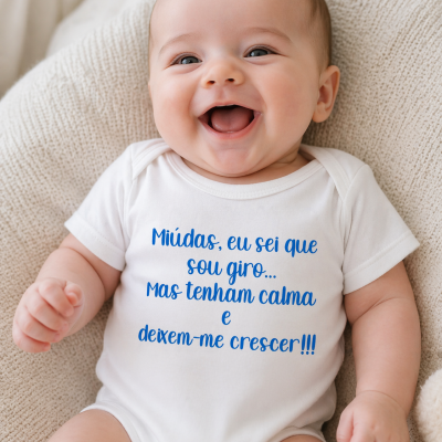 Body de bebé branco com texto azul sentado num tecido bege texturizado