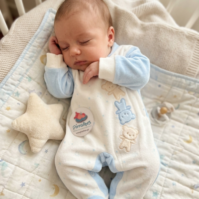 Pijama de bebé branco e azul com ursinhos bordados num colchão com padrão espacial e almofada em estrela creme