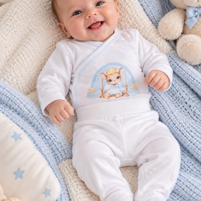 Bebé sorridente vestido com conjunto branco estampado, deitado sobre mantas de malha azul e bege, junto a ursinho de peluche.