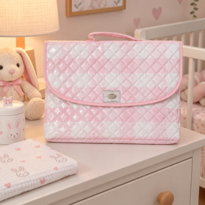 Bolsa de maternidade rosa e branca acolchoada sobre cómoda em ambiente de quarto de bebé.