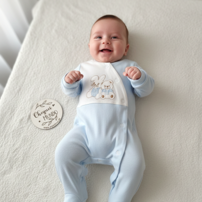 Bebé com macacão azul claro e branco com bordado de coelho e urso deitado em manta branca com placa redonda ao lado