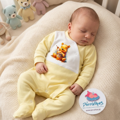 Bebé dorme com macacão amarelo com estampa de ursinho no mel, almofada bege de malha e cartão promocional ao lado