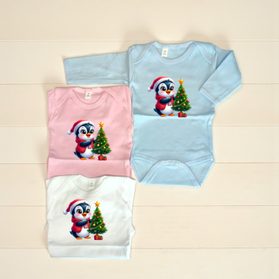 Bodies infantis azul claro, rosa e branco com estampa natalícia de pinguim decorando árvore de Natal.