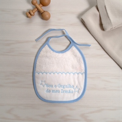 Babete branco com detalhes azuis e bordado texto em português sobre superfície de madeira clara