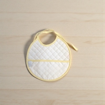 Babete de bebé acolchoado branco com bordas amarelas em superfície de madeira clara