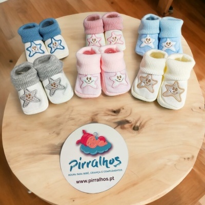 Cinco pares de meias de bebé coloridas com estrelas sorridentes, em cima de uma mesa de madeira com logótipo de marca.