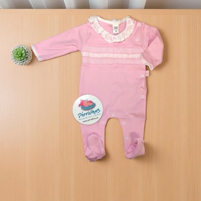 Pijama rosa para bebé com gola de renda branca e botões, sobre mesa de madeira clara com planta suculenta