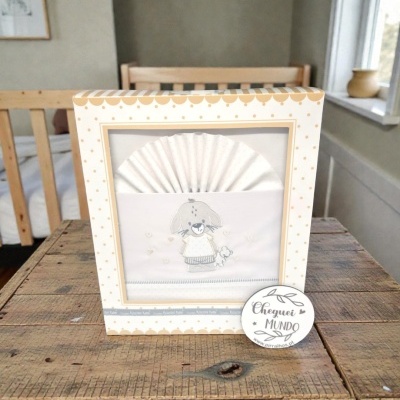 Caixa de manta ou roupa de bebé branca com bordado de cão e caixa com pontos bege sobre mesa de madeira.