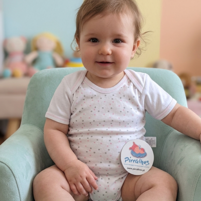 Bebé sentado numa poltrona azul clara a usar body branco com estrelas cinza e rosa e etiqueta Pirralhos