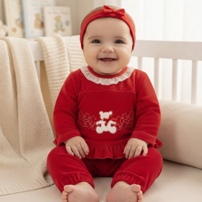 Bebé vestido com fato de veludo vermelho com aplicação de urso branco, sentado em ambiente interior claro