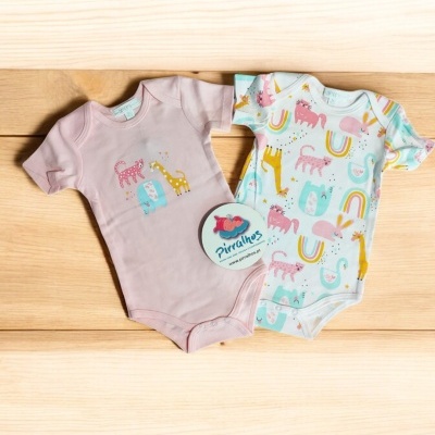 Dois bodies de bebé com estampados coloridos sobre superfície de madeira clara