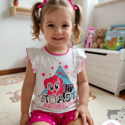 Menina sentada a usar pijama branco e rosa com personagem e texto, quarto infantil com brinquedos e tapete ilustrado