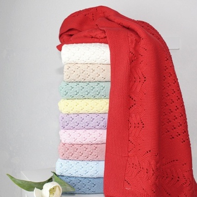 Empilhamento de mantas coloridas de tricot com padrões perforados e flor branca ao lado.