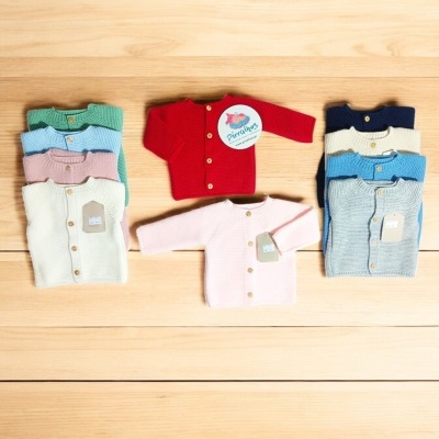 Camisolas de malha para bebé em várias cores com botões e etiquetas sobre madeira clara