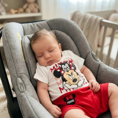 Bebé adormecido numa cadeirinha de carro cinza com roupa da Minnie Mouse.