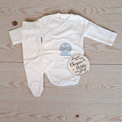 Conjunto de roupa de bebé branco com bordado azul sobre superfície de madeira clara