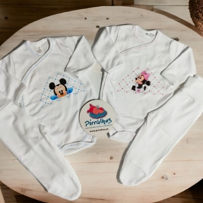 Fatos de bebé brancos com estampas Mickey e Minnie sobre mesa de madeira clara