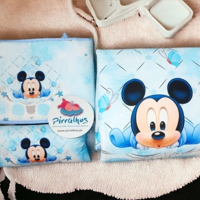 Três artigos de tecido azul claro com estampas do personagem Mickey Mouse colocados sobre uma superfície macia cor de rosa