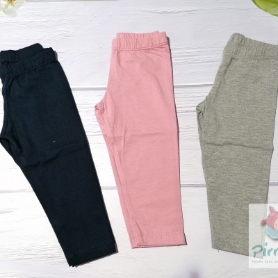 Três calças de criança em preto, rosa e cinza, em superfície branca de madeira com decoração floral