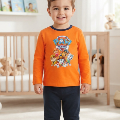 Menino em pijama laranja com personagem PAW PATROL e calças azuis escuras em quarto infantil