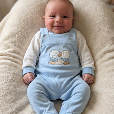 Bebé sorridente sentado com macacão azul claro e camisola branca