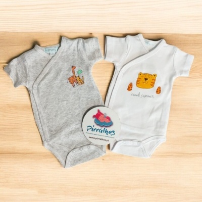 Dois bodys de bebé cinzento com girafa e branco com tigre, em fundo de madeira