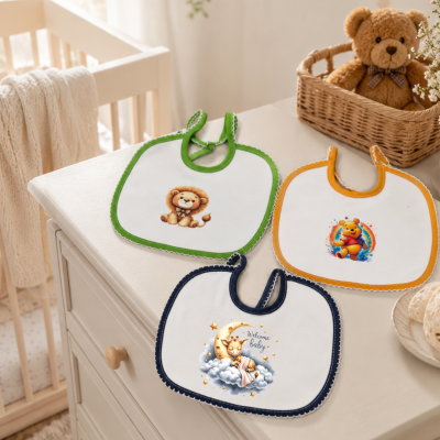 Três babetes brancos com desenhos infantis e bordas coloridas sobre uma cómoda branca com um urso de peluche na cesta ao lado.