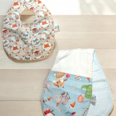 Dois babetes de bebé com padrões animais coloridos sobre madeira clara