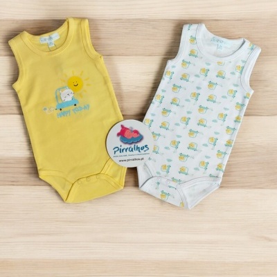 Dois bodies de bebé, amarelo e branco com desenhos de sol e carro, sobre mesa de madeira clara.