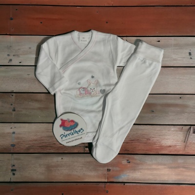 Conjunto de roupa branca para bebé com bordado de coelho sobre fundo de tábuas de madeira