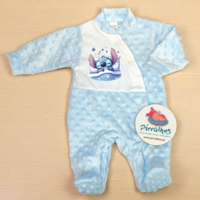 Macacão azul claro com estampa de personagem e etiqueta redonda em superfície de madeira clara