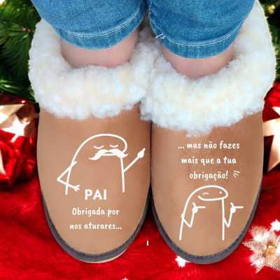Chinelos castanhos com pelúcia branca interior e texto em português, usados com calças azuis em tapete vermelho natalício