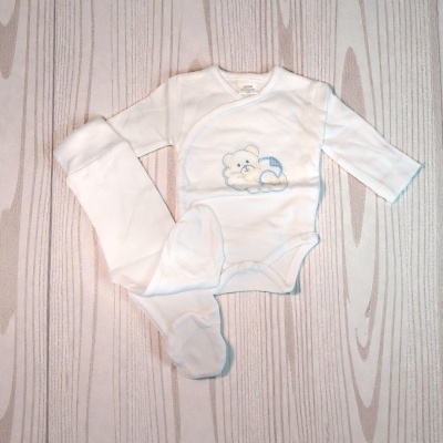 Conjunto de roupa de bebé branca com body e calças com pés sobre fundo de madeira clara