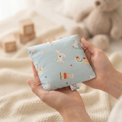 Almofada pequena azul com desenhos de coelho e arco-íris nas mãos de uma pessoa
