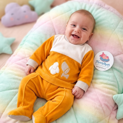 Bebé de fato mostarda posado em almofada macia colorida com almofadas em forma de nuvem e estrelas