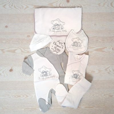 Conjunto de roupa para bebé branco e cinza com bordado de ursinhos e texto em tecido, exposto sobre fundo de madeira clara.