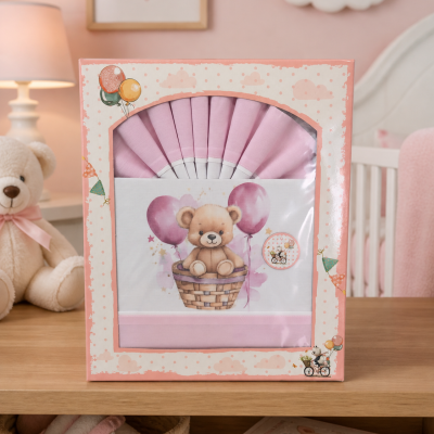 Jogo de cama infantil rosa com ursinho e balões na embalagem colocada numa mesa de madeira num quarto cor-de-rosa