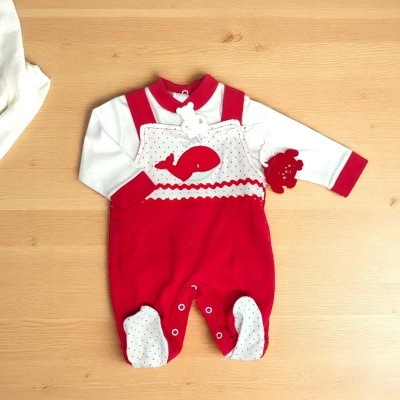 Macacão de bebé vermelho e branco com padrão de bolinhas e baleia, sobre fundo de madeira
