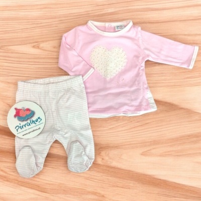 Conjunto de roupa de bebé rosa e branca com coração e riscas sobre madeira