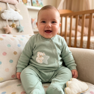 Bebé a sorrir vestido com babygrow verde água sentado num sofá com padrão de pontos coloridos