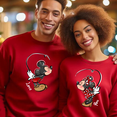 Casal jovem com camisolas vermelhas estampadas com Mickey e Minnie Mouse em ambiente interior iluminado.
