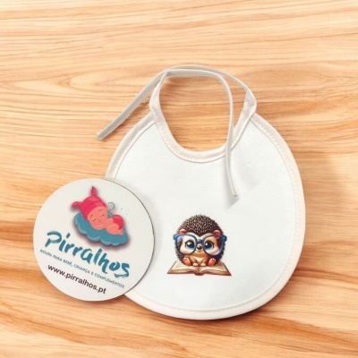 Babete branco com padrão de porco-espinho com óculos azuis a ler um livro e etiqueta com marca Pirralhos sobre madeira clara